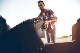 man putting suitcase into trunk